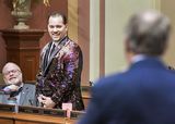 Blurred in the foreground, Representative Torkelson looks at Representative Lucero, who is standing in front of him and smiling at him.